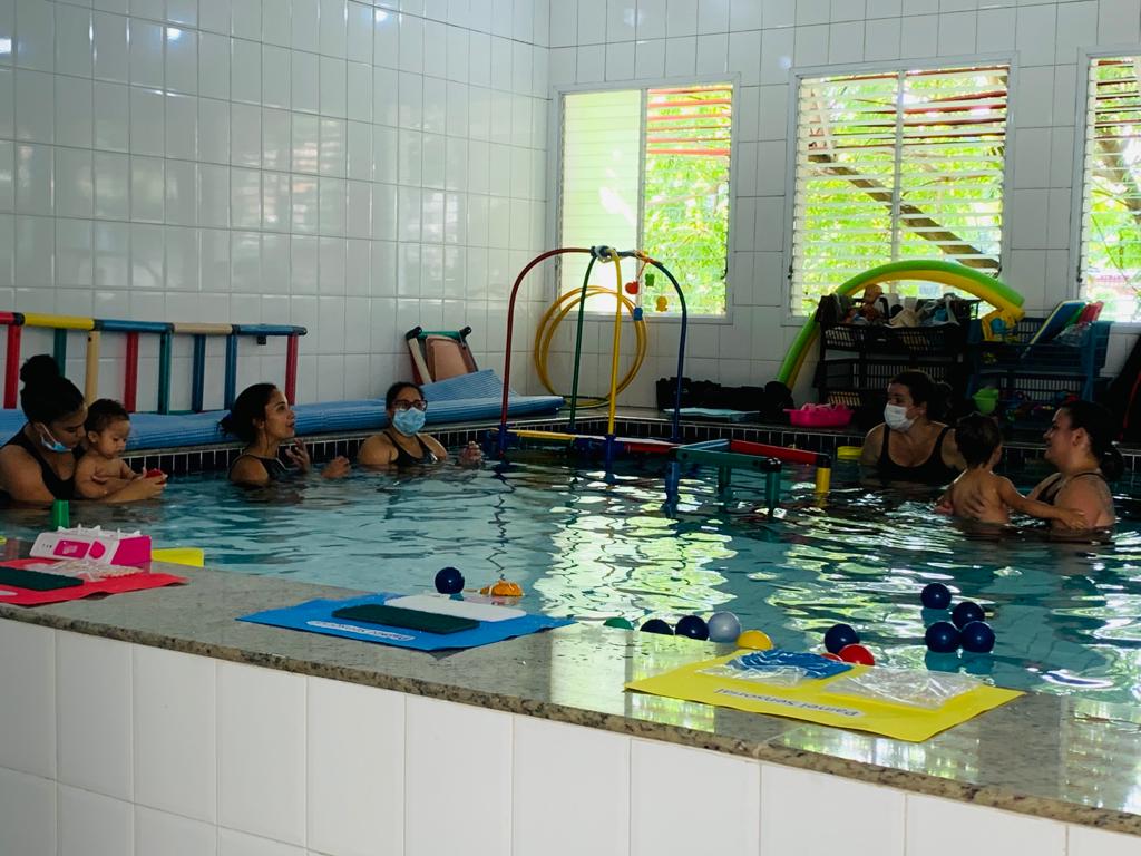 A foto mostra um grupo de mulheres e crianças em uma piscina